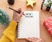Woman,Hand,Writing,New,Year's,Resolution,On,Note,Paper,In