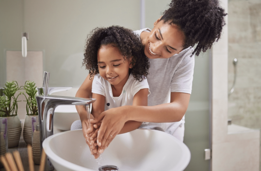 A woman and child practicing good hygiene by washing their hands together in a sink.